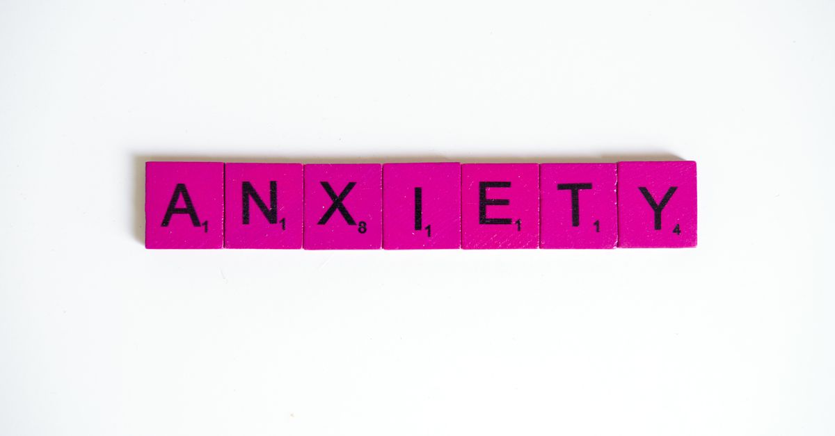 Pink Scrabble tiles spelling 'anxiety' on a white surface. Concept of mental health.