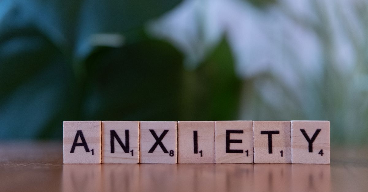 Close-up of wooden blocks spelling ANXIETY on a wooden surface with blurred green background.