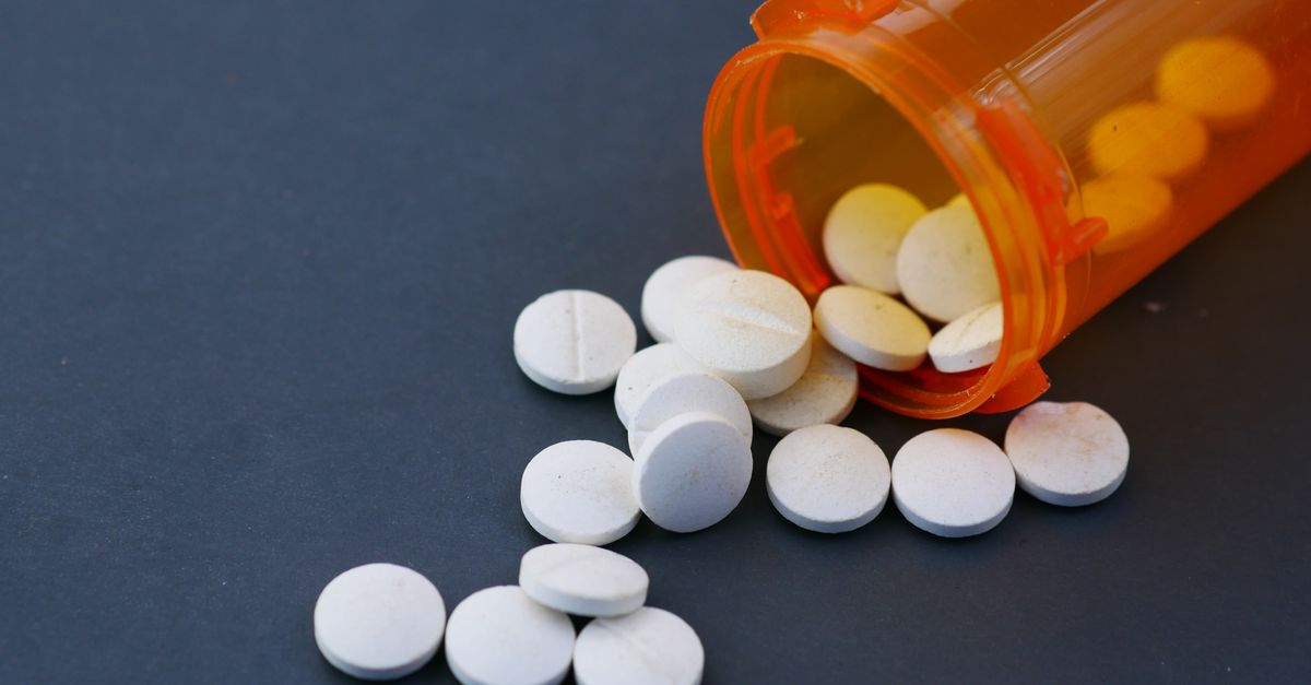 Close-up of white pills scattered from an orange prescription bottle on a gray surface.