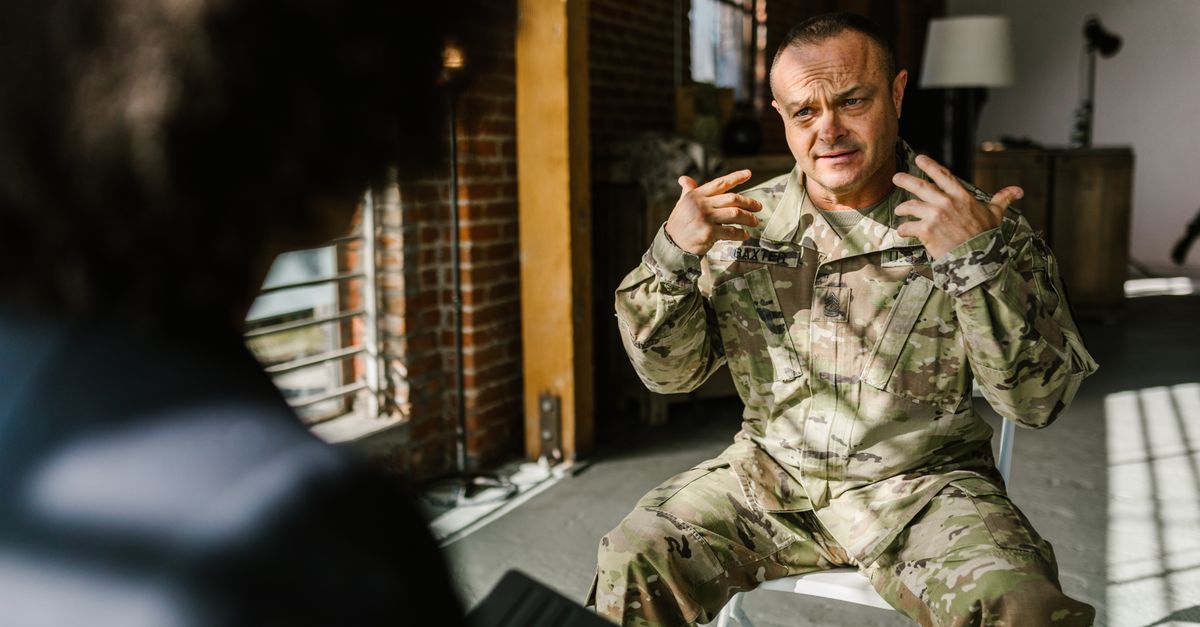 A combat veteran in military uniform engages in a counseling session indoors, expressing emotions.