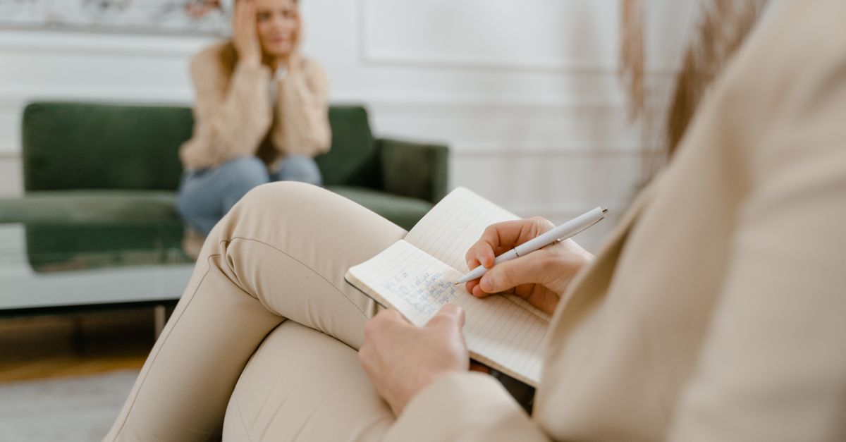 A therapist taking notes during a consultation with a patient, focusing on mental health.