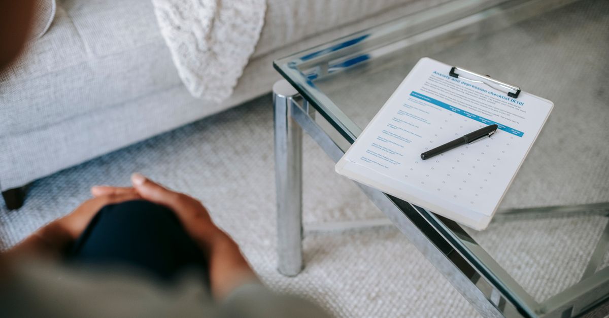 From above of blurred unrecognizable female psychologist sitting in office near table with clipboard and pen during session in office