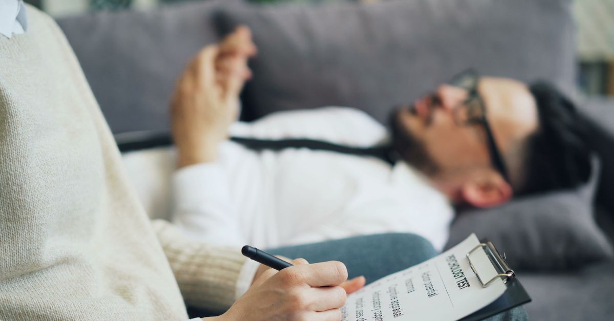 A client discusses issues during a therapy session with a therapist taking notes, indoors.
