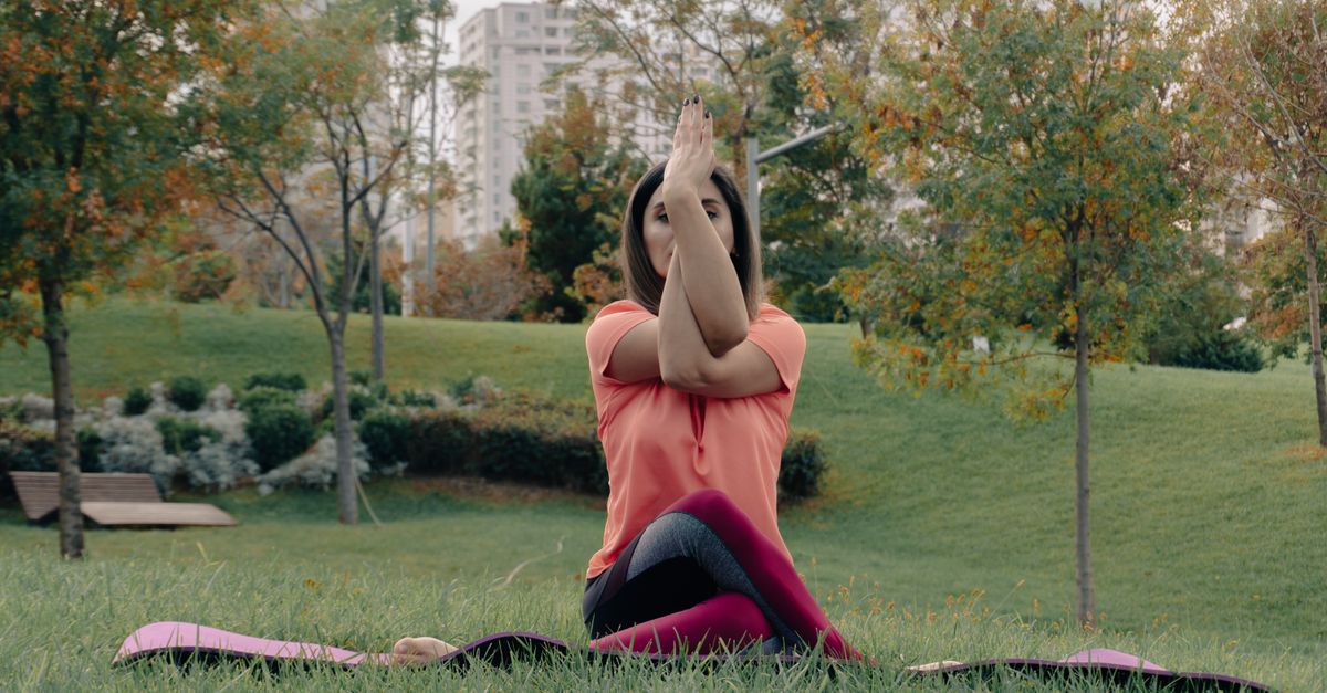 A woman performing a yoga pose on a mat in an urban park setting during fall.