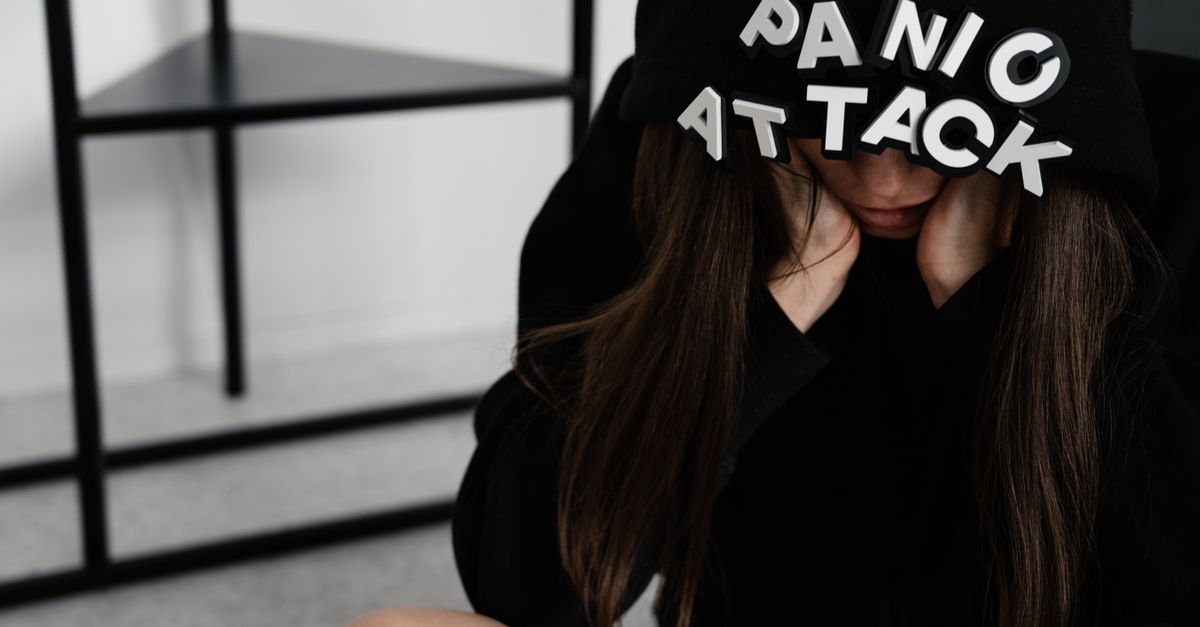 A woman sitting with 'PANIC ATTACK' on her hood, showing anxiety indoors.