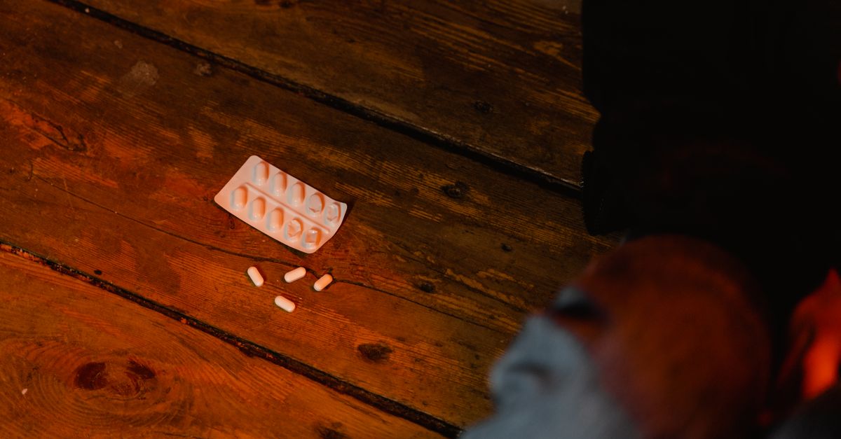 Close-up view of scattered white pills and empty blister pack on a wooden surface, suggesting concepts of medicine or mental health.