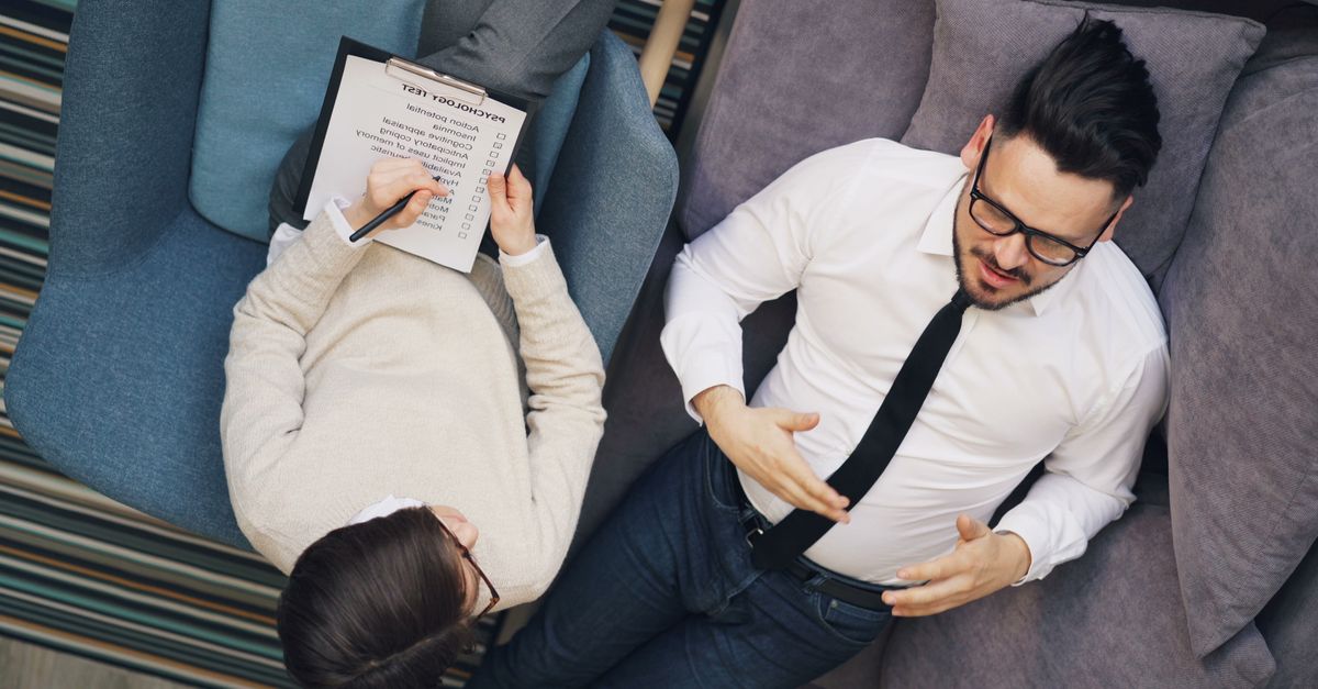 Therapist takes notes while patient discusses problems on a couch during a session.