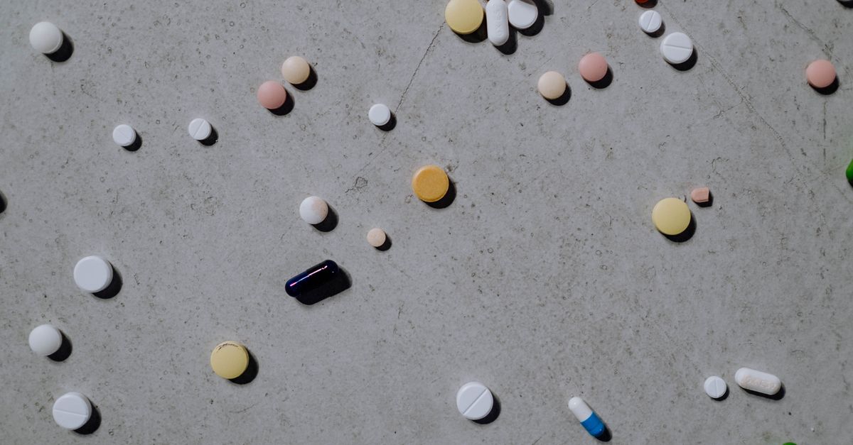 Varied colorful pills and tablets scattered on a grey surface, viewed from above.