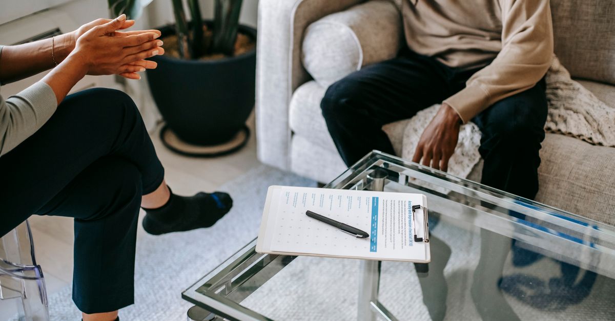 Crop anonymous African American man in casual clothes sitting on sofa and talking to female psychologist during psychotherapy session in modern studio