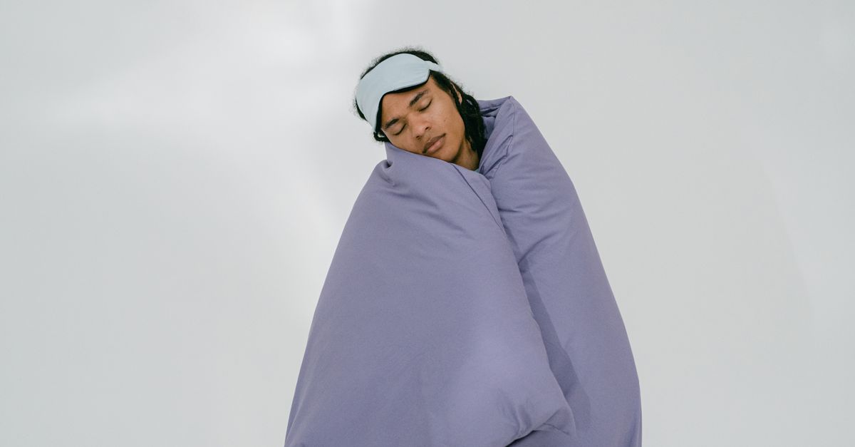 A person peacefully sleeping with an eye mask, wrapped in a purple blanket on a white background.