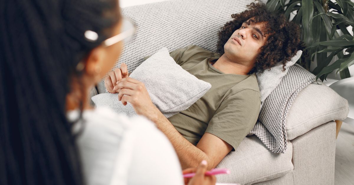Man lying on couch during therapy session with female therapist taking notes.