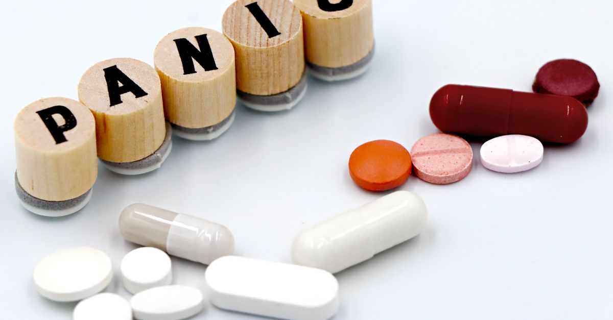 Assorted pills arranged beside wooden tiles spelling 'PANIC', symbolizing anxiety treatment.