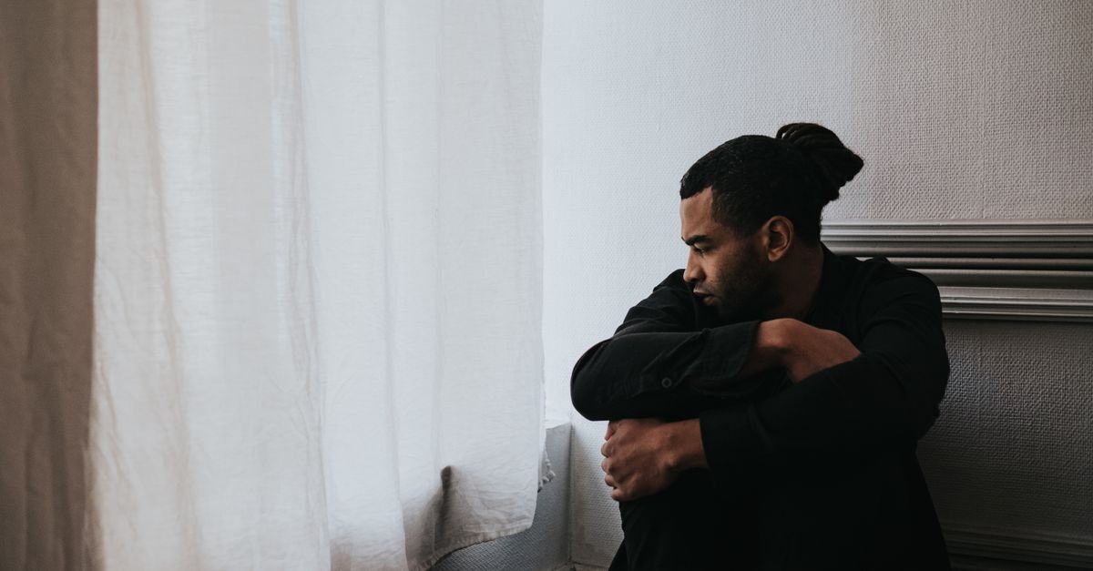 A man sits alone by a window, reflecting on emotions in a minimalist room.