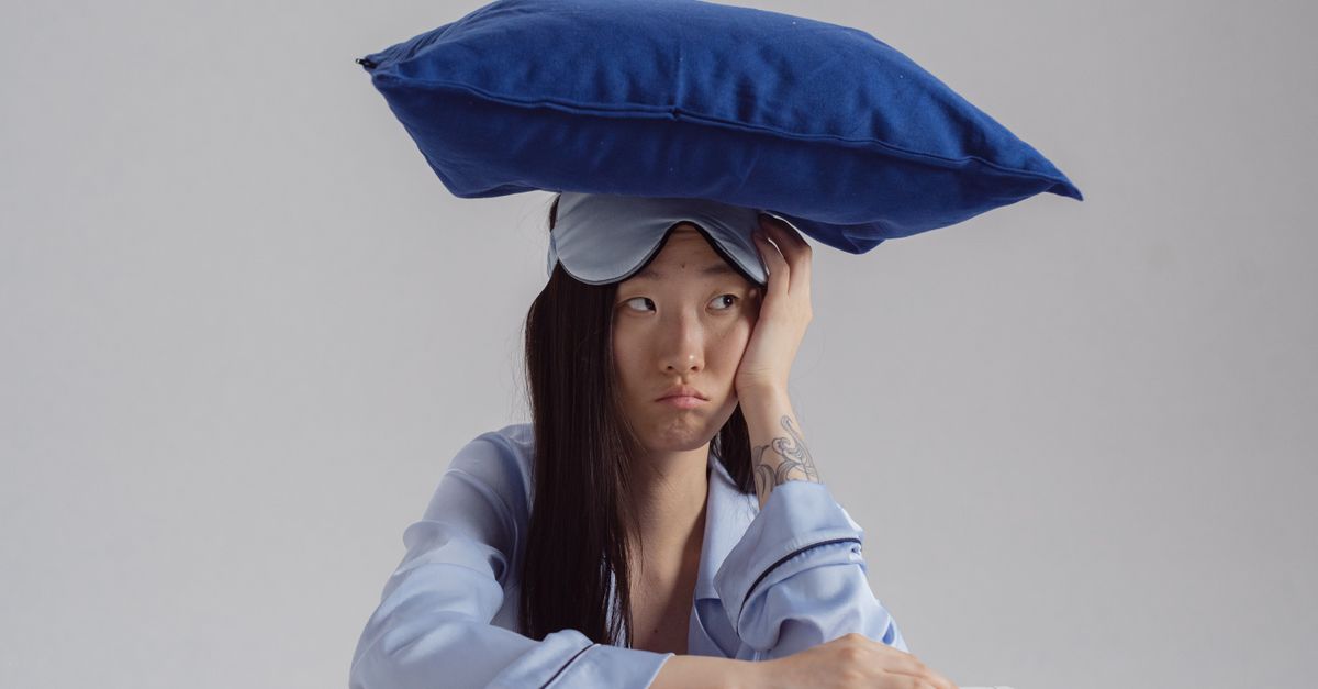 Tattooed woman with pillow and sleep mask showing insomnia concept.